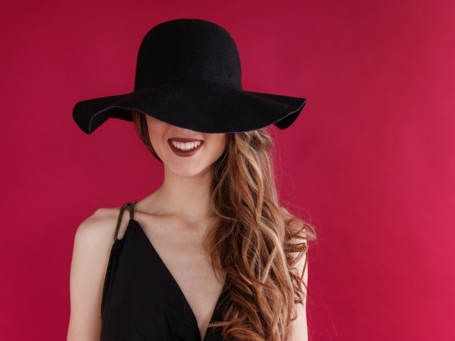 Черная шляпа на лице у девушки на розовом фоне