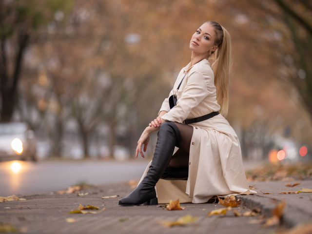 Девушка блондинка сидит в пальто в парке