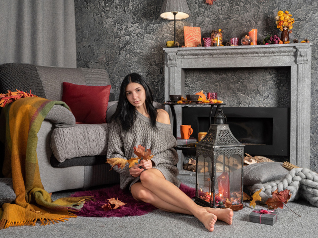 Милая девушка в теплом свитере сидит в комнате с камином