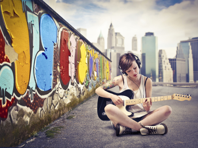 Девушка с гитарой сидит у стены