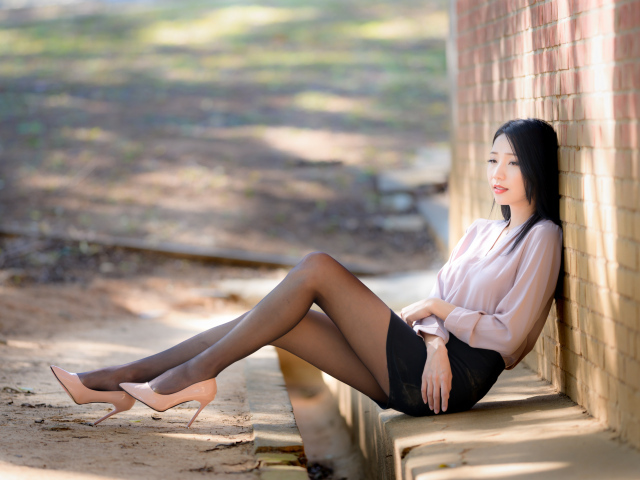 Грустная азиатка сиди у кирпичной стены