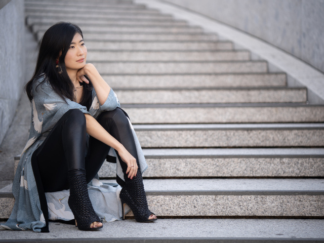 Задумчивая девушка азиатка сидит на ступеньках