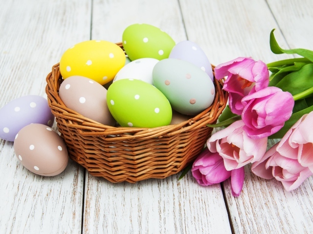 Корзина разноцветных яиц с тюльпанами на столе на Пасху