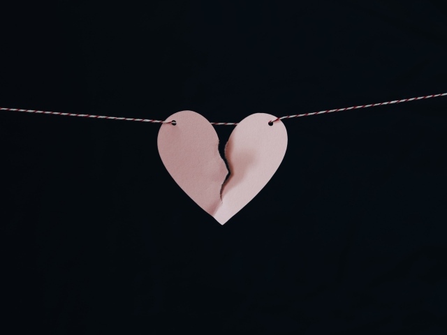Разорванное бумажное сердце на нитке на черном фоне