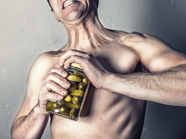 Мужчина открывает банку огурцов