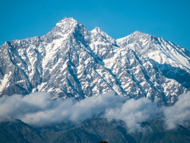 Высокие заснеженные горы в тумане под голубым небом