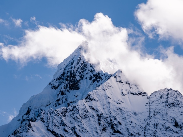 Острая заснеженная вершина горы в белых облаках