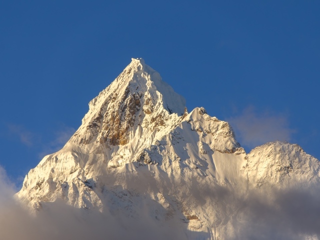 Крутая заснеженная вершина горы на голубом фоне