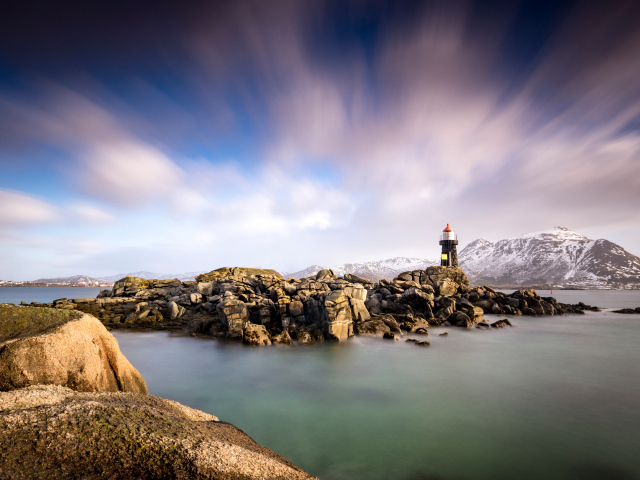 Маяк стоит на каменном берегу на фоне гор