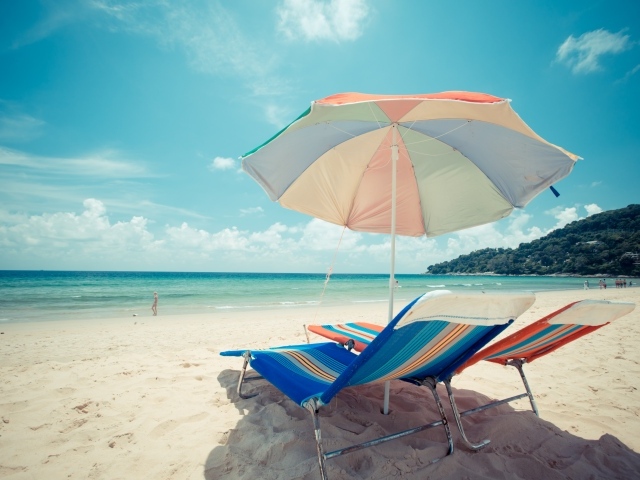 Шезлонги и разноцветный зонт на пляже летом
