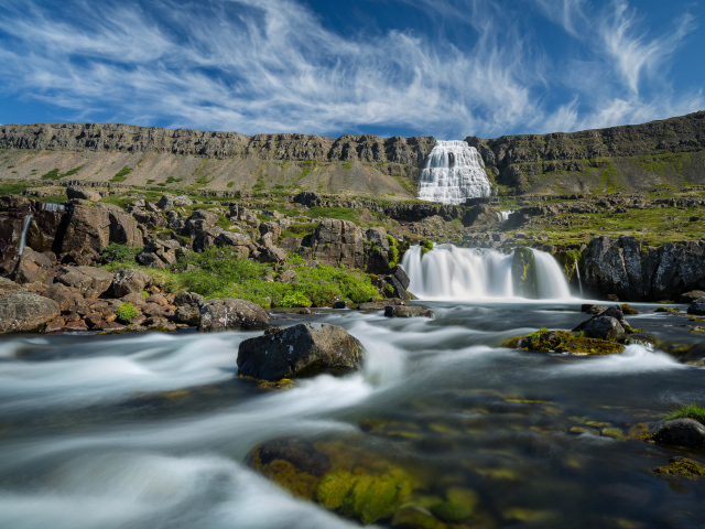 Водопад стекает с гор на фоне красивого голубого неба Исландии