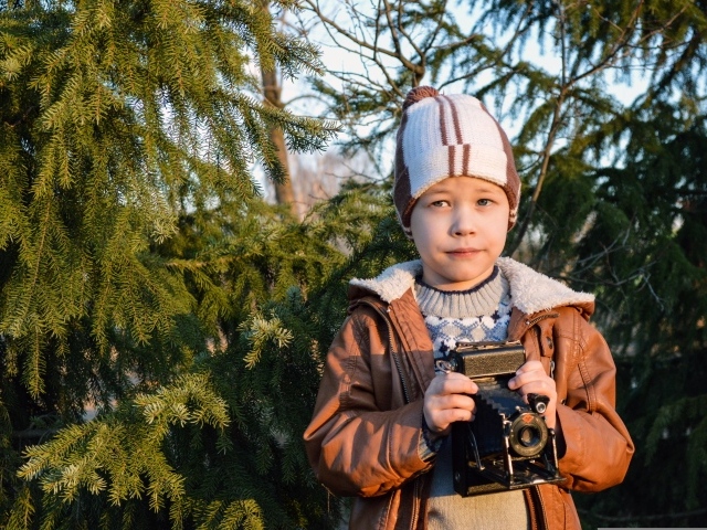 Мальчик с фотоаппаратом стоит у ели