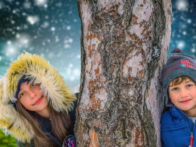 Мальчик и девочка стоят у дерева зимой