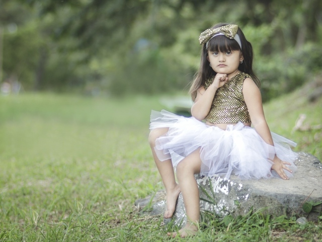 Девочка в красивом платье сидит на камне