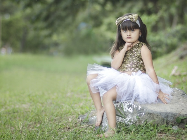 Девочка в красивом платье сидит на камне