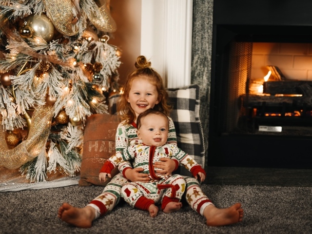 Маленькие брат и сестра сидят у новогодней ели