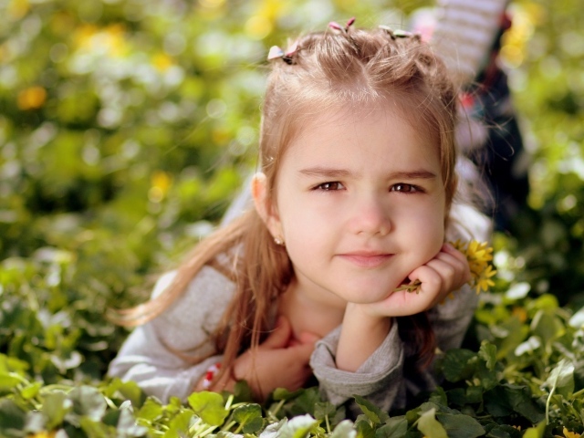 Маленькая кареглазая девочка лежит на траве с цветами