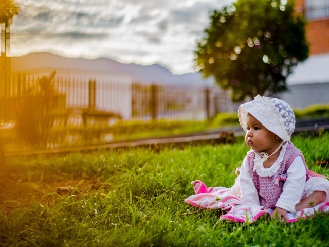 Маленькая девочка в розовом платье сидит на траве