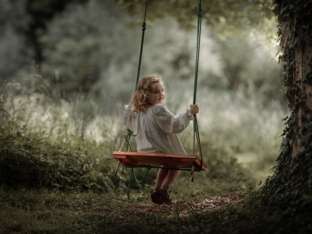 Маленькая девочка на качели в саду