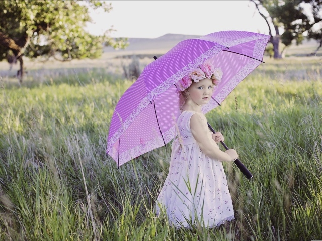 Маленькая девочка стоит в траве с зонтом