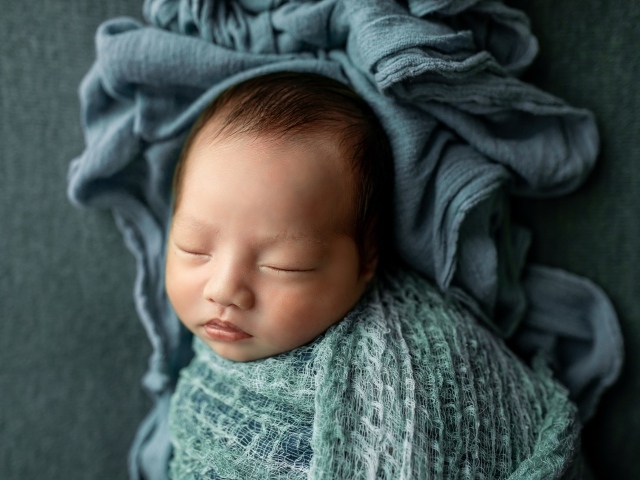 Новорожденный ребенок завернут в серое покрывало 