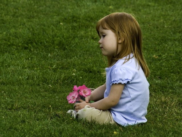 Грустная маленькая девочка сидит на зеленой траве 