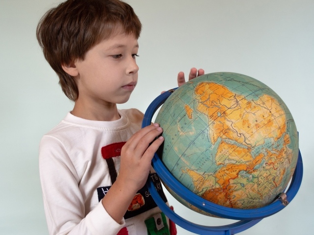 Школьник изучает глобус на сером фоне