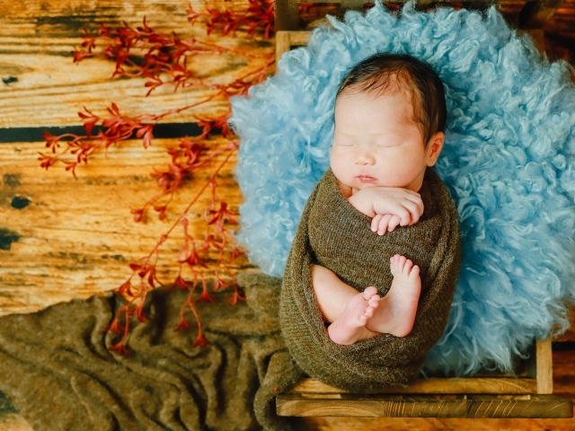 Крошечный новорожденный ребенок на голубой меховой подушке