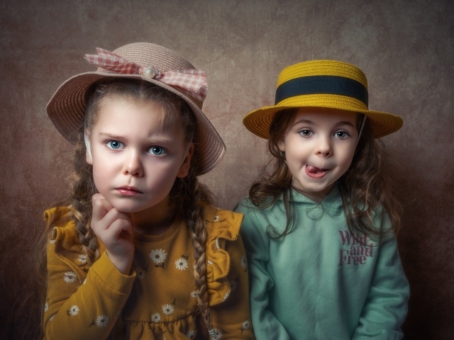 Две маленькие девочки в шляпках на фоне коричневой стены