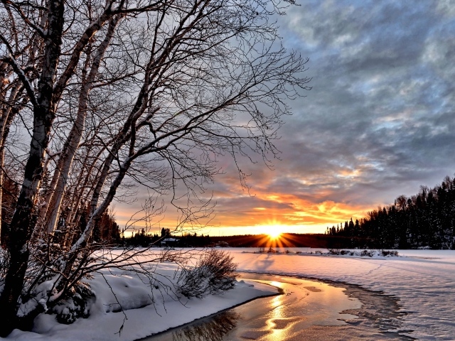 Яркое зимнее солнце на рассвете над заледеневшей рекой