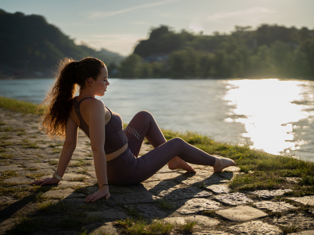 Спортивная девушка сидит на берегу реки