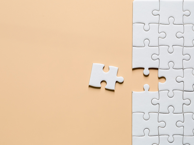 Белый пазл собирают на бежевом фоне