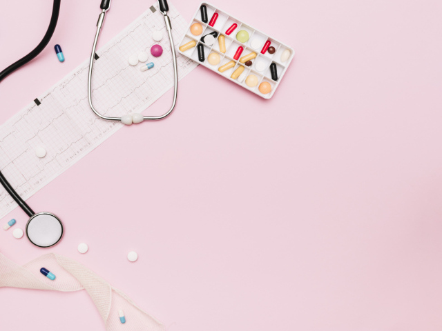 Стетоскоп и лекарства на кардиограмме на розовом фоне