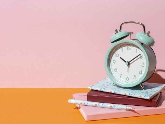 Будильник с книгами на розовом фоне