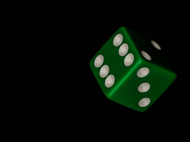 Зеленый игральный кубик на черном фоне