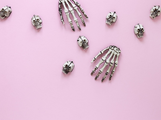 Кисти рук скелета и черепа на розовом фоне