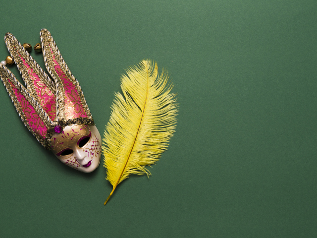 Венецианская маска и желтое перо на зеленом фоне