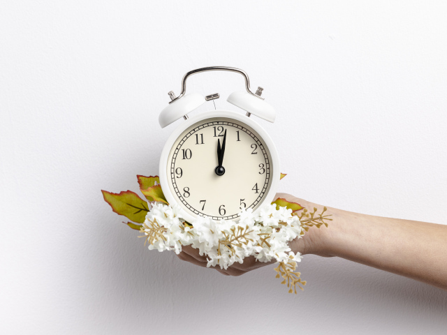 Белый будильник в руке с цветами на сером фоне