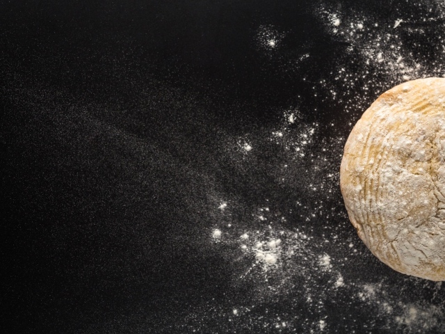 Сырое тесто на черном столе с мукой