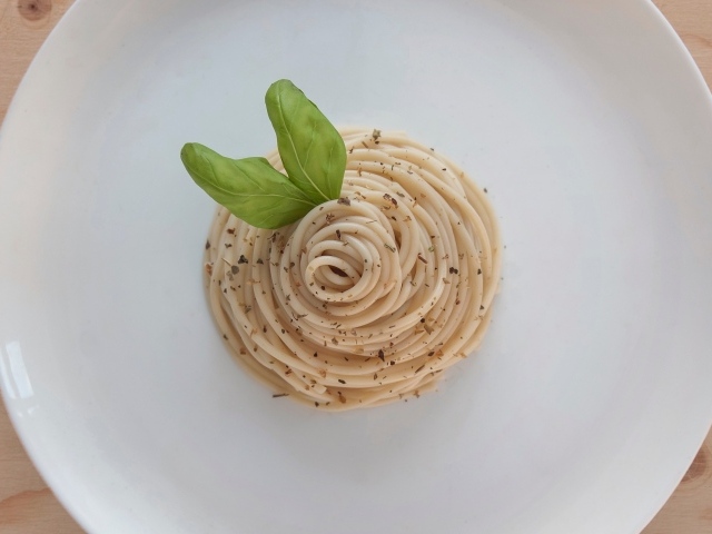 Спагетти с листьями базилика на белой тарелке