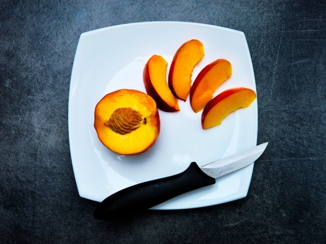 Нарезанный персик на белой тарелке
