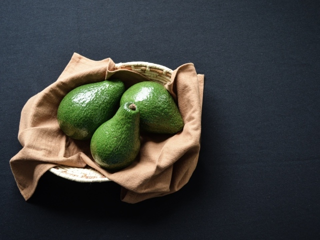 Три зеленых авокадо в корзинке на столе