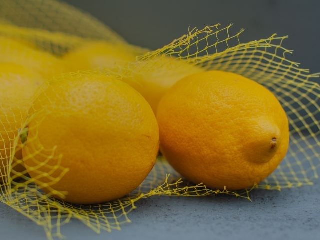Желтые лимоны в сетке на сером столе
