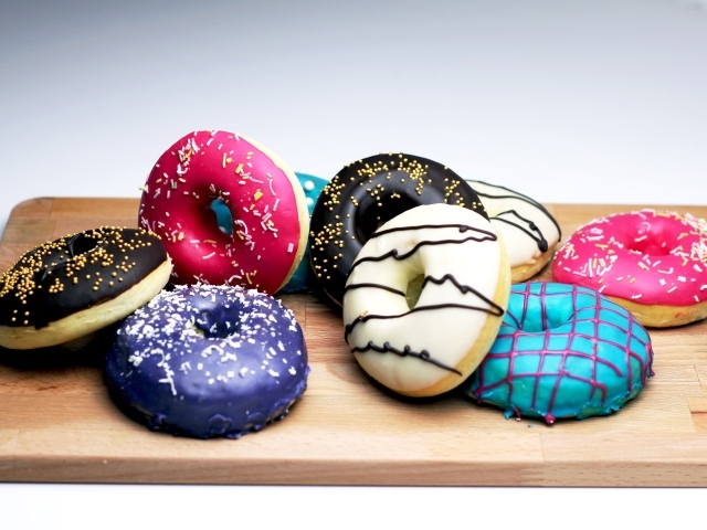 Аппетитные разноцветные пончики на деревянной доске