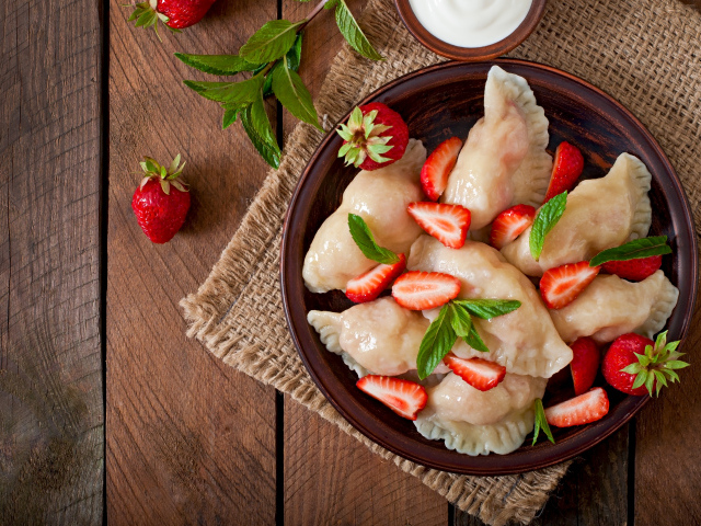 Вареники с клубникой на столе со сметаной