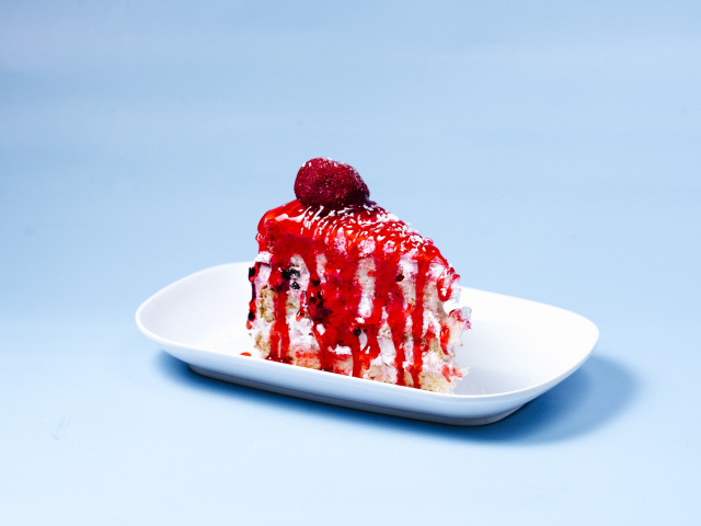 Кусок торта с клубничным сиропом на голубом фоне