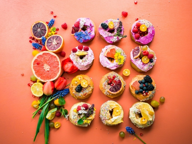 Сладкие пончики на оранжевом фоне с фруктами и цветами
