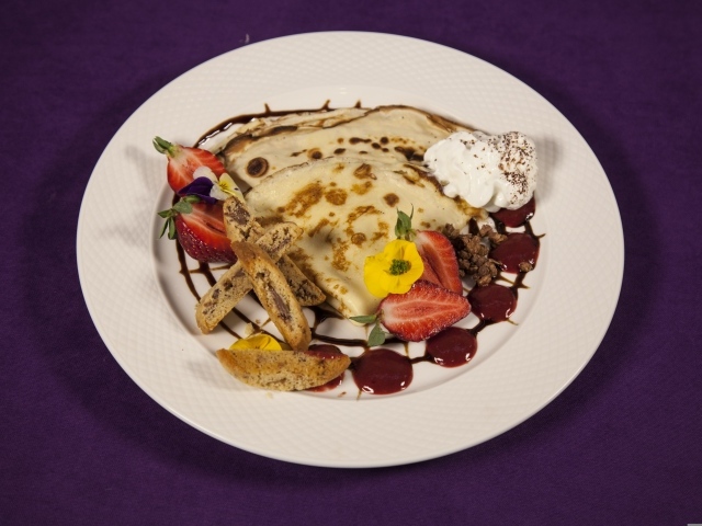 Тонкие блинчики с кремом и ягодами на тарелке