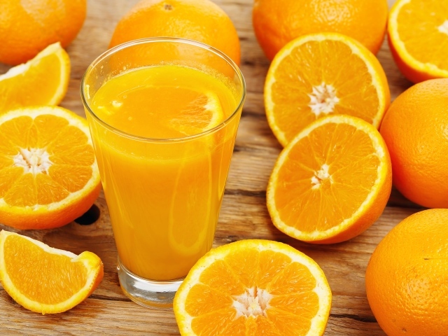 Стакан свежевыжатого сока на столе с половинками апельсина