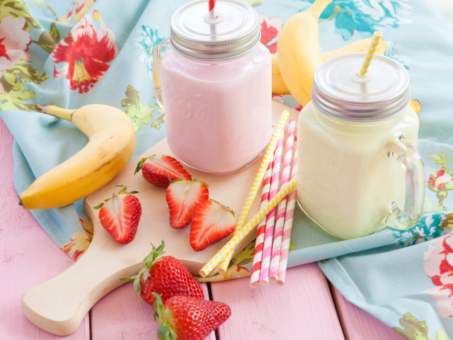 Две банки смузи на столе с бананом и ягодами клубники